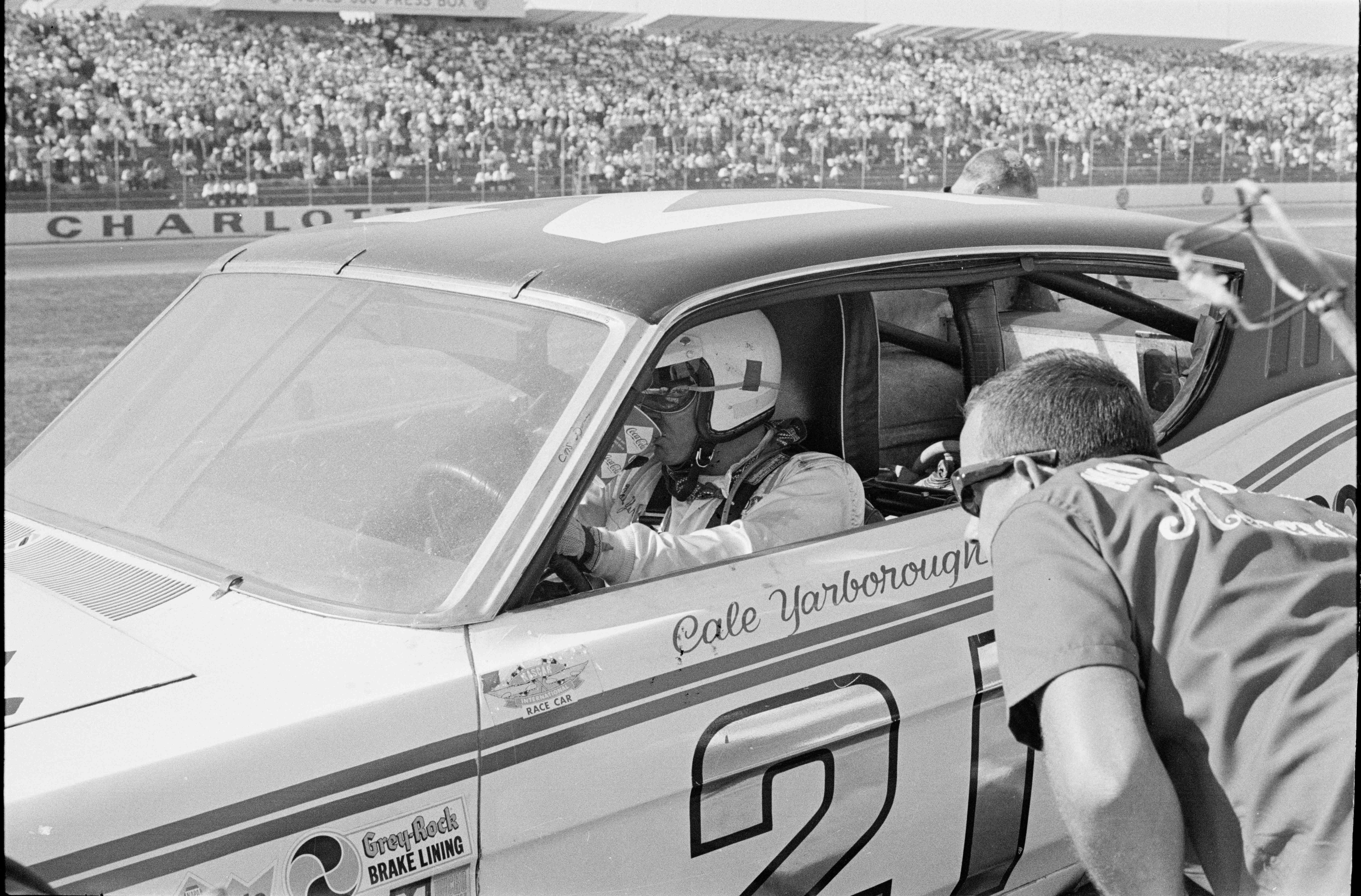 Cale Yarborough takes a drink at a pit stop during the 1969 National 500 at the Charlotte Motor Speedway while a member of the pit crew looks on