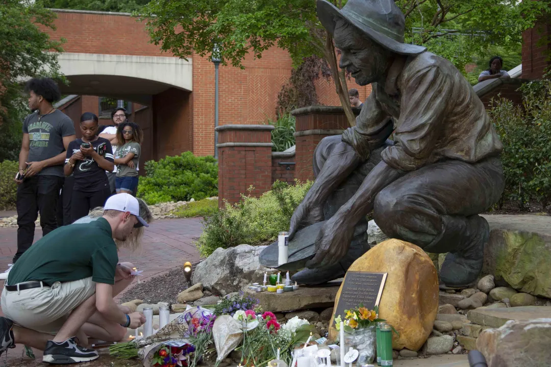 Students placing memorial items and lighting candles at the Niner Miner statue